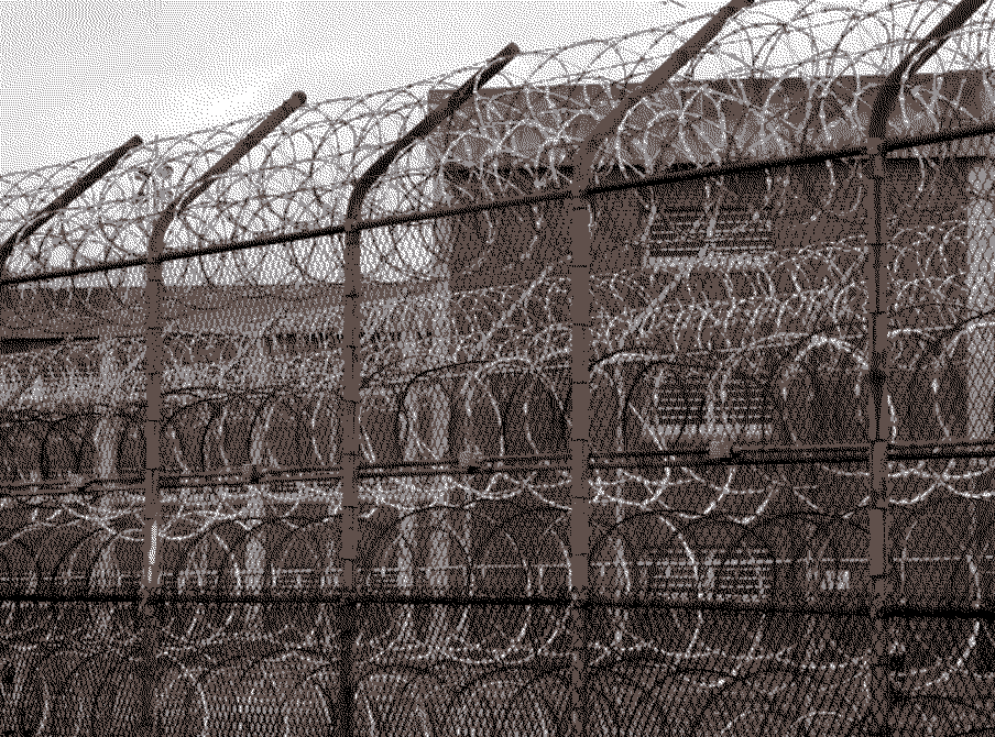 A barbed wire fence outside of a brick prison building.