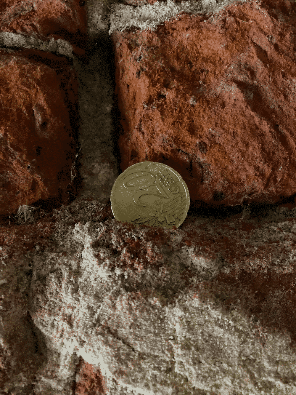 A coin rests in a notch in some brick, up close.