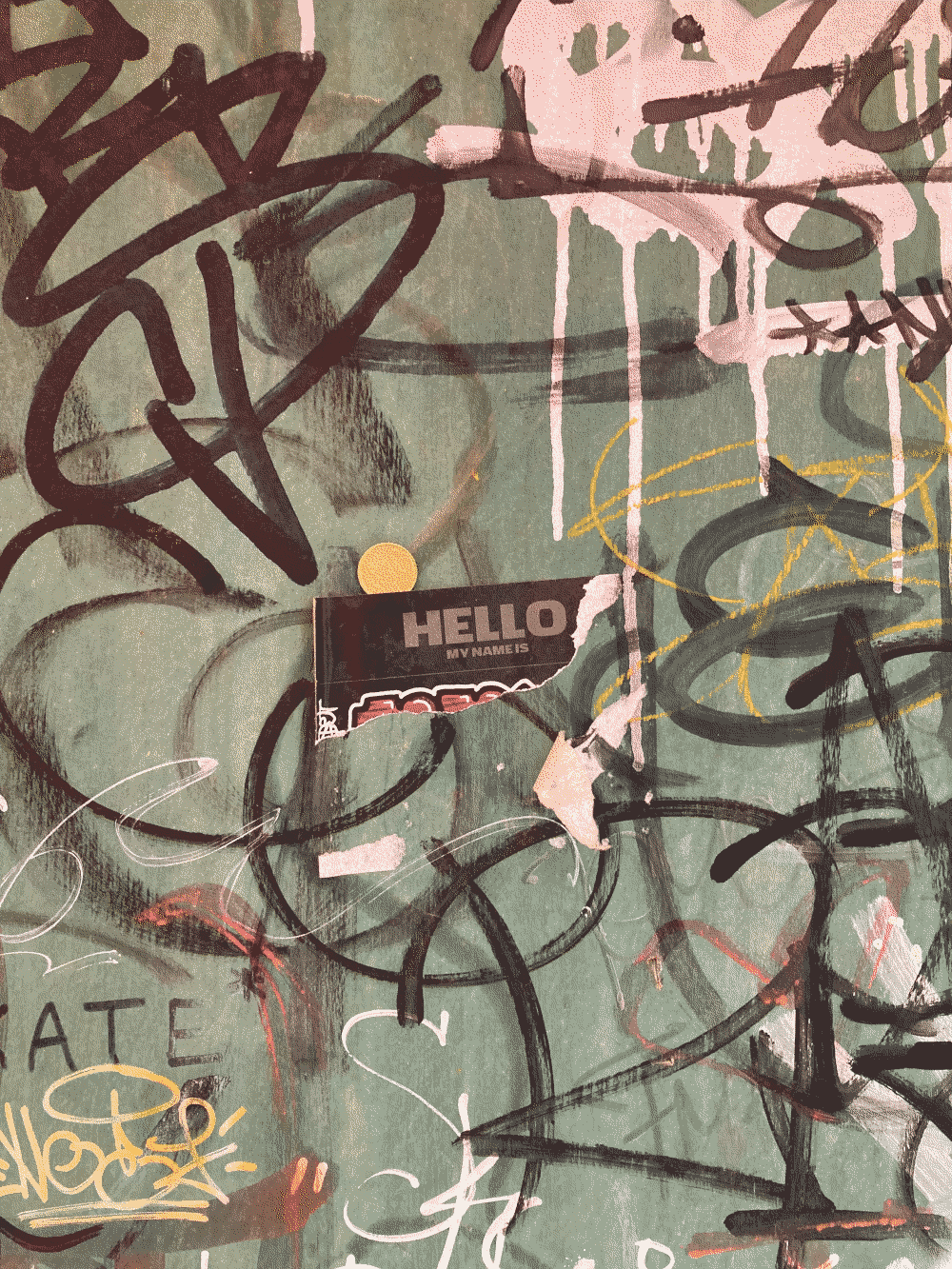 A coin is partway slipped behind a sticker reading HELLO, which is itself peeling off a graffiti-covered door.