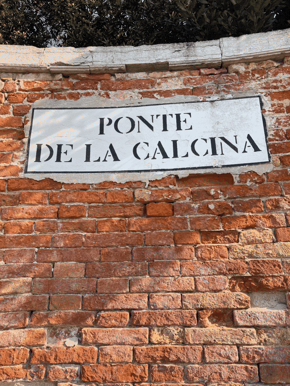 A coin is hidden in a brick wall with the street name PONTE DE LA CALCINA painted on it.