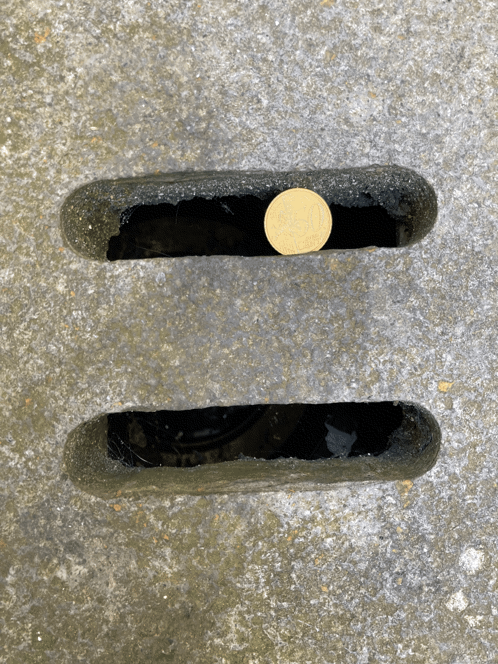 A coin sits stuck in a drain below the ground.