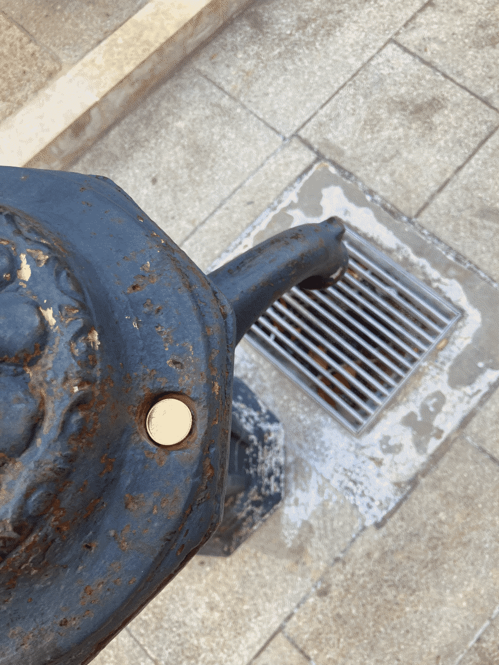 A coin sits in the large bolt hole at the edge of a public water spout.