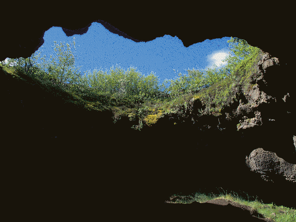 The sky is visible through a crevice entrance above, the photographer shooting from below.